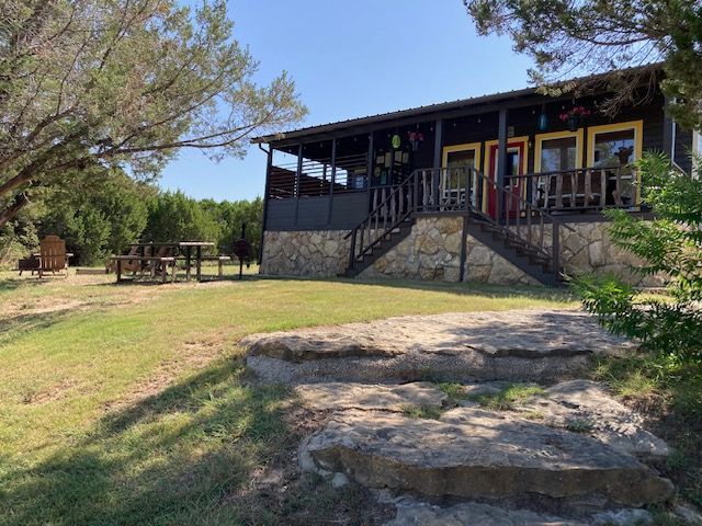 Cabin with stone steps on a grassy hillside, trees and picnic tables in the foreground.