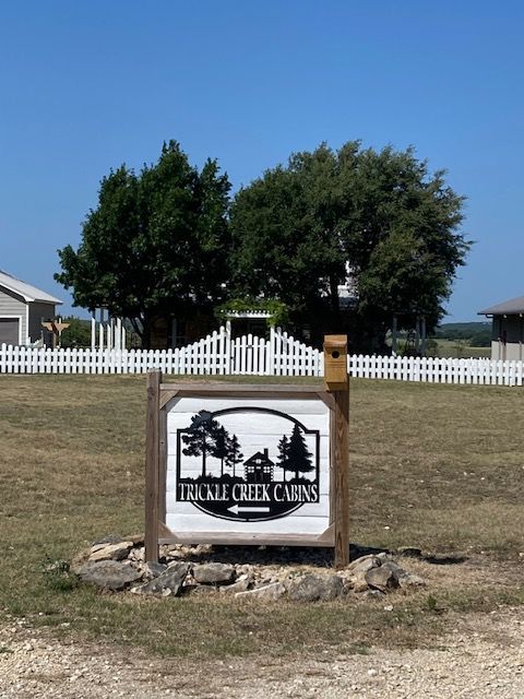 Palm tree ranch sign in a grassy field with white fence and trees under a clear blue sky
