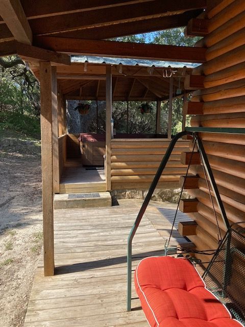 Wooden porch with railing, red cushioned chair, and a covered walkway beside a rustic cabin.