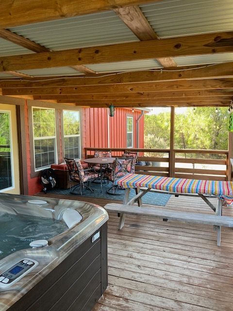 Covered deck with hot tub, seating, and striped lounge chairs overlooking a red building and greenery