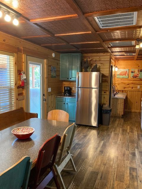 Cozy wood-paneled kitchen and dining area with stainless steel fridge, blue cabinets, and a table by windows