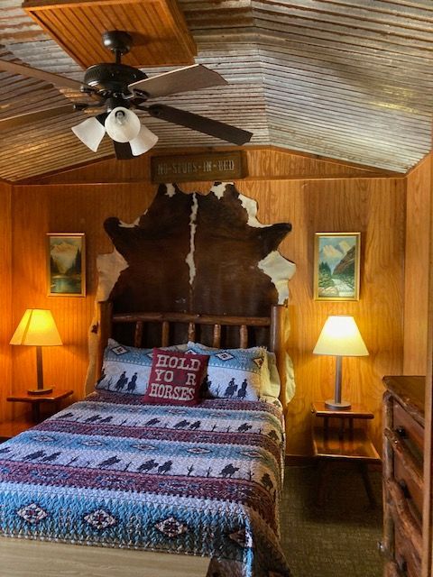 Cozy wood-paneled bedroom with a bed, lamps, ceiling fan, and rustic decor