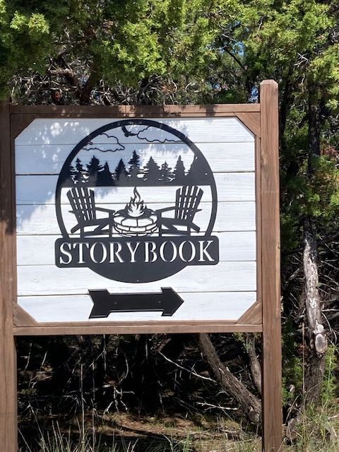 Wooden Storybook sign with a black forest silhouette and arrow pointing right in a wooded area