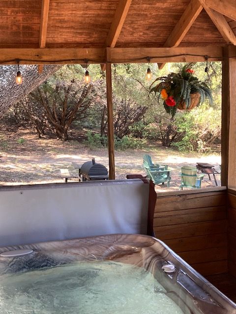 Wooden gazebo with a hot tub overlooking a sunny backyard garden