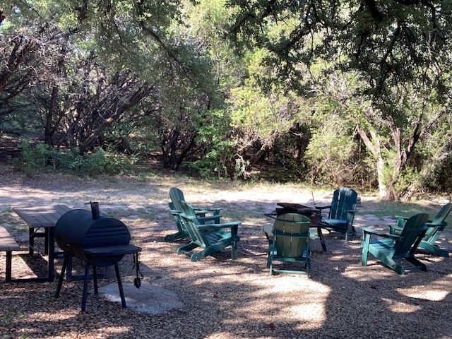 Outdoor campsite with a grill and several green chairs in a shaded wooded clearing