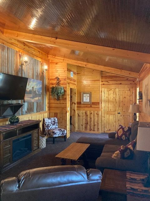 Cozy log cabin living room with wood-paneled walls, fireplace, sofa, TV, and rustic decor
