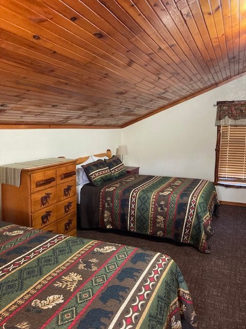 Cozy attic bedroom with two patterned beds, wooden dresser, and sloped wood ceiling