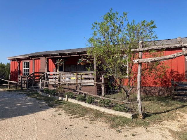 Red building with wooden porch and fence beside a dirt path under a clear blue sky