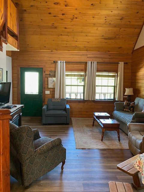 Cozy wood-paneled living room with green door, large windows, and dark armchairs around a coffee table