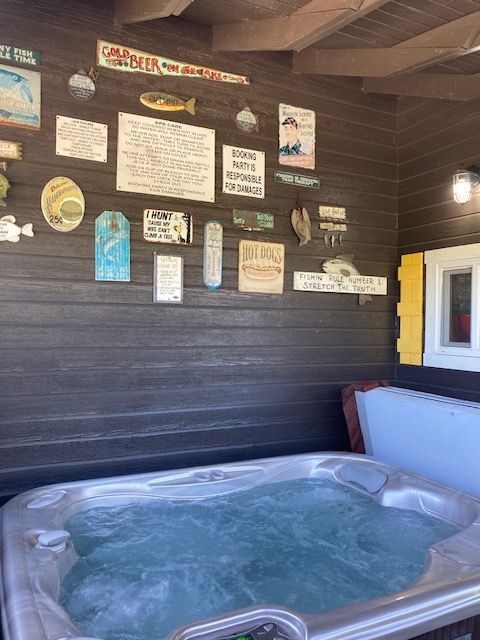 Hot tub on a covered patio beside a black wall with decorative signs and a bench.