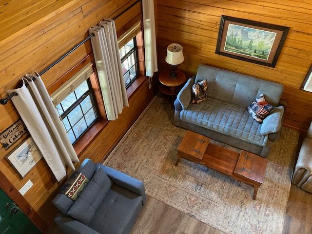 Cozy living room with a blue sofa, armchair, coffee table, lamp, rug, and large windows.