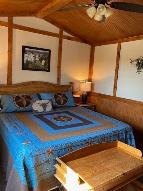 Cozy bedroom with a blue quilted bedspread, wood-paneled walls and ceiling, and a small bench at the foot of the bed