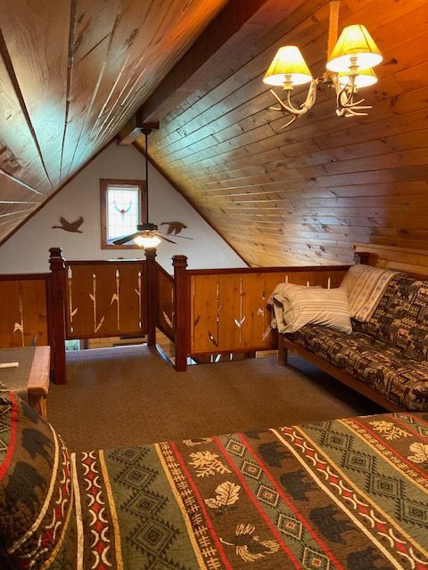 Cozy attic sitting room with wood-paneled walls, patterned rug, sofa, and warm ceiling lights