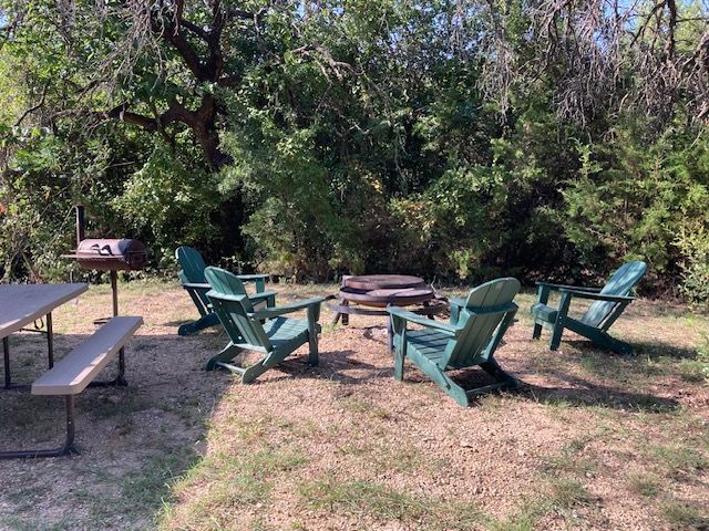 Green chairs around a fire pit in a wooded outdoor seating area