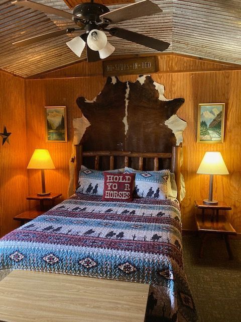 Rustic bedroom with carved headboard, patterned bedspread, warm lamps, and wood-paneled walls