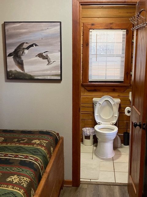 Bedroom with an attached bathroom, showing a bed, dolphin wall art, and a toilet in a small tiled room.