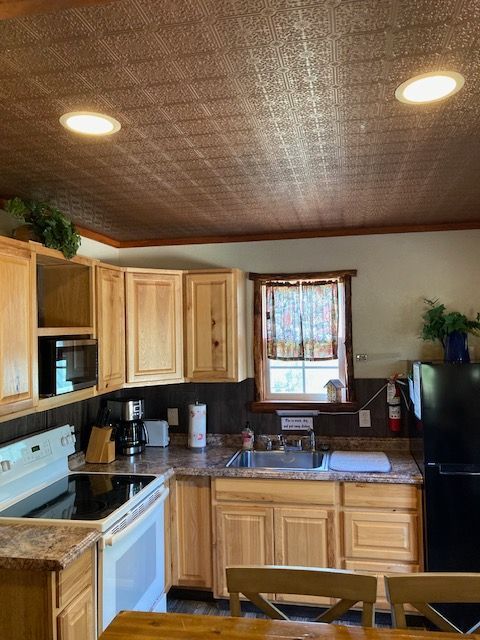 Kitchen interior with wood cabinets, white stove, sink under window, and warm ceiling lights