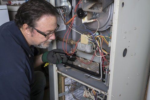 Man in glasses inspecting furnace components. He is wearing gloves and working in a utility room.