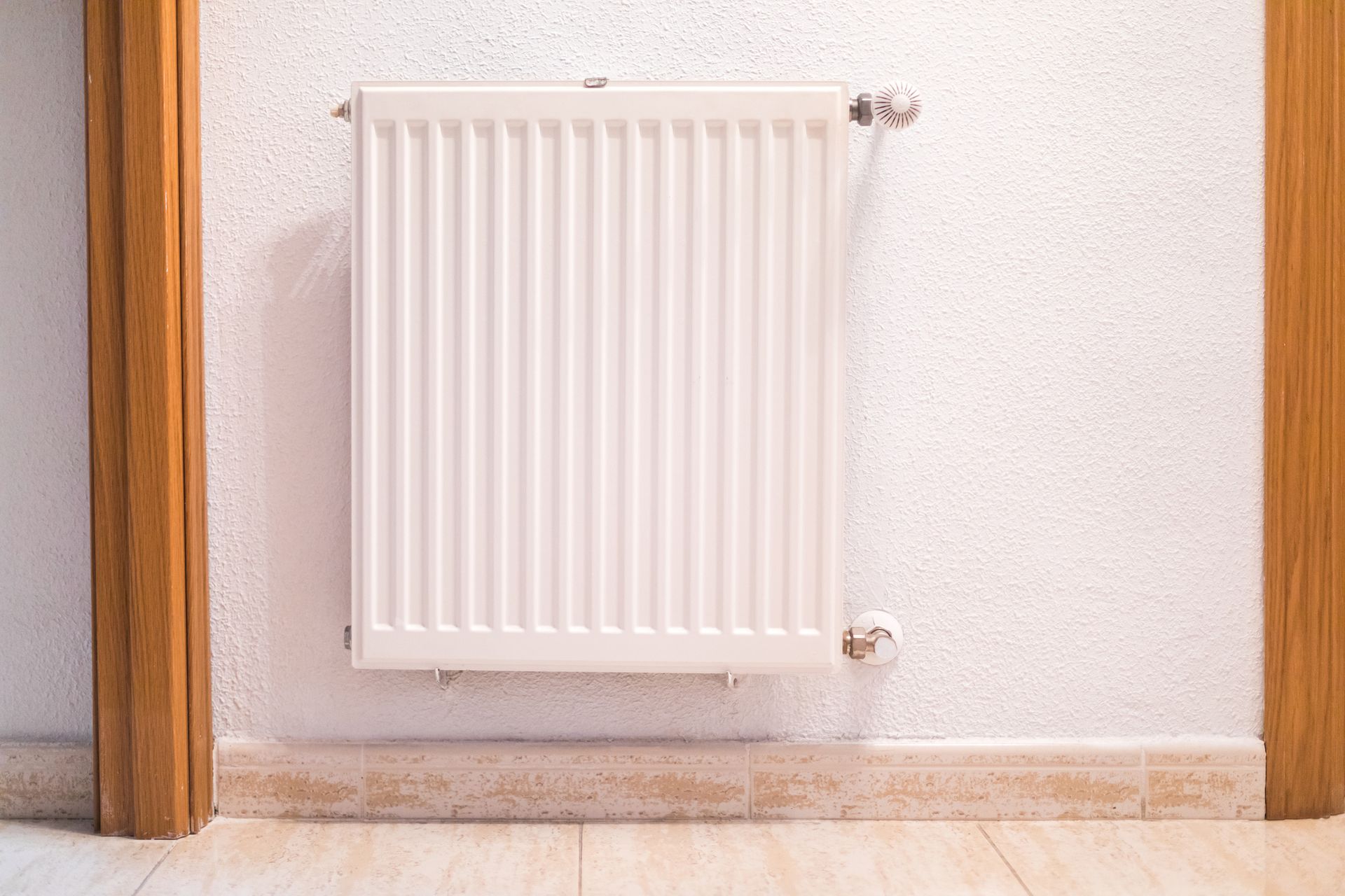 White wall-mounted radiator heater between two wooden door frames on a tiled floor.