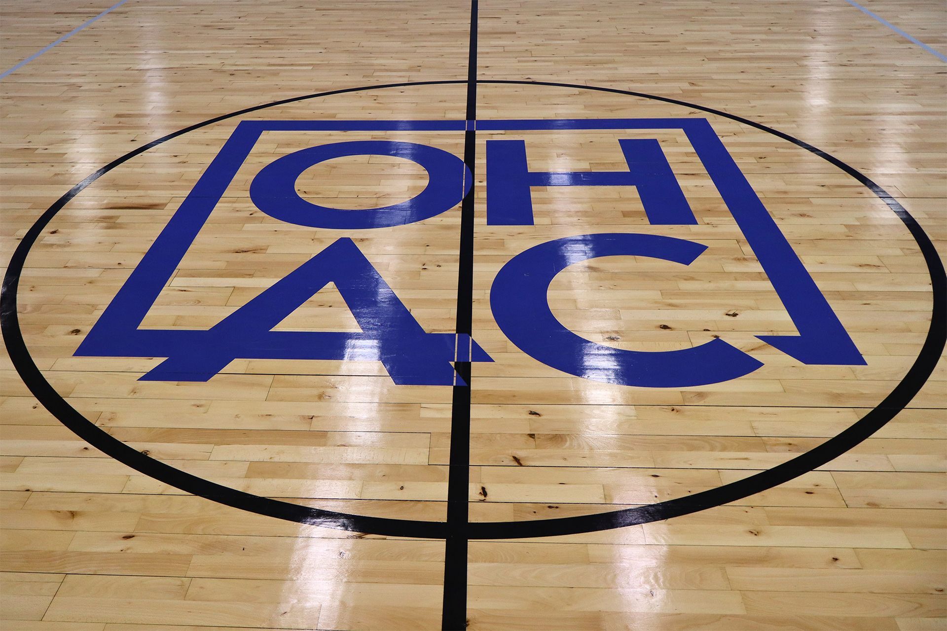 Blue Greek letters on a wooden gym floor inside a black center-circle court marking.