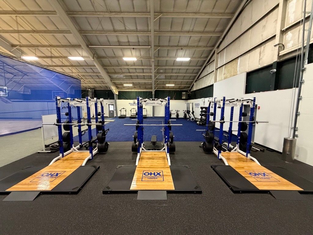 Indoor gym with several blue workout stations and orange mats lined up on a black floor