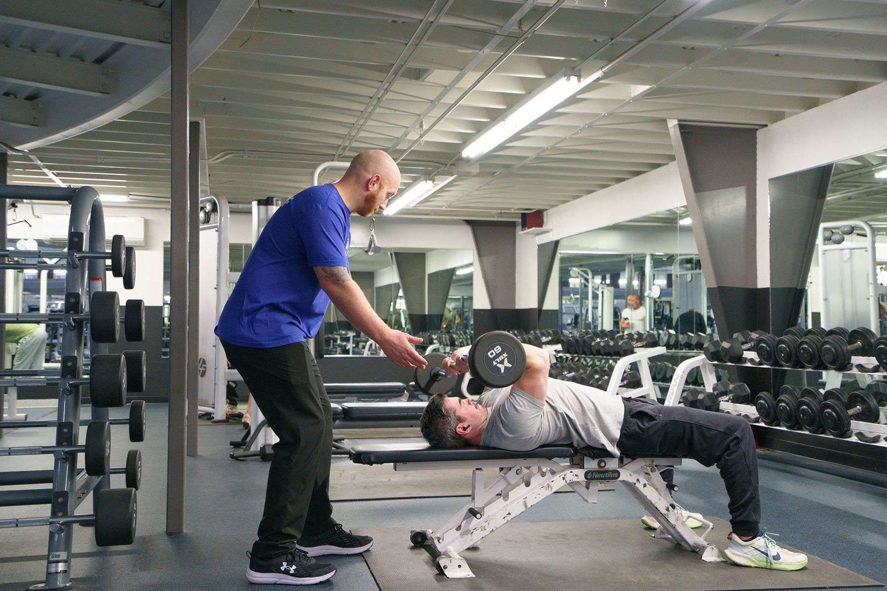 A man is lifting a dumbbell on a bench in a gym.