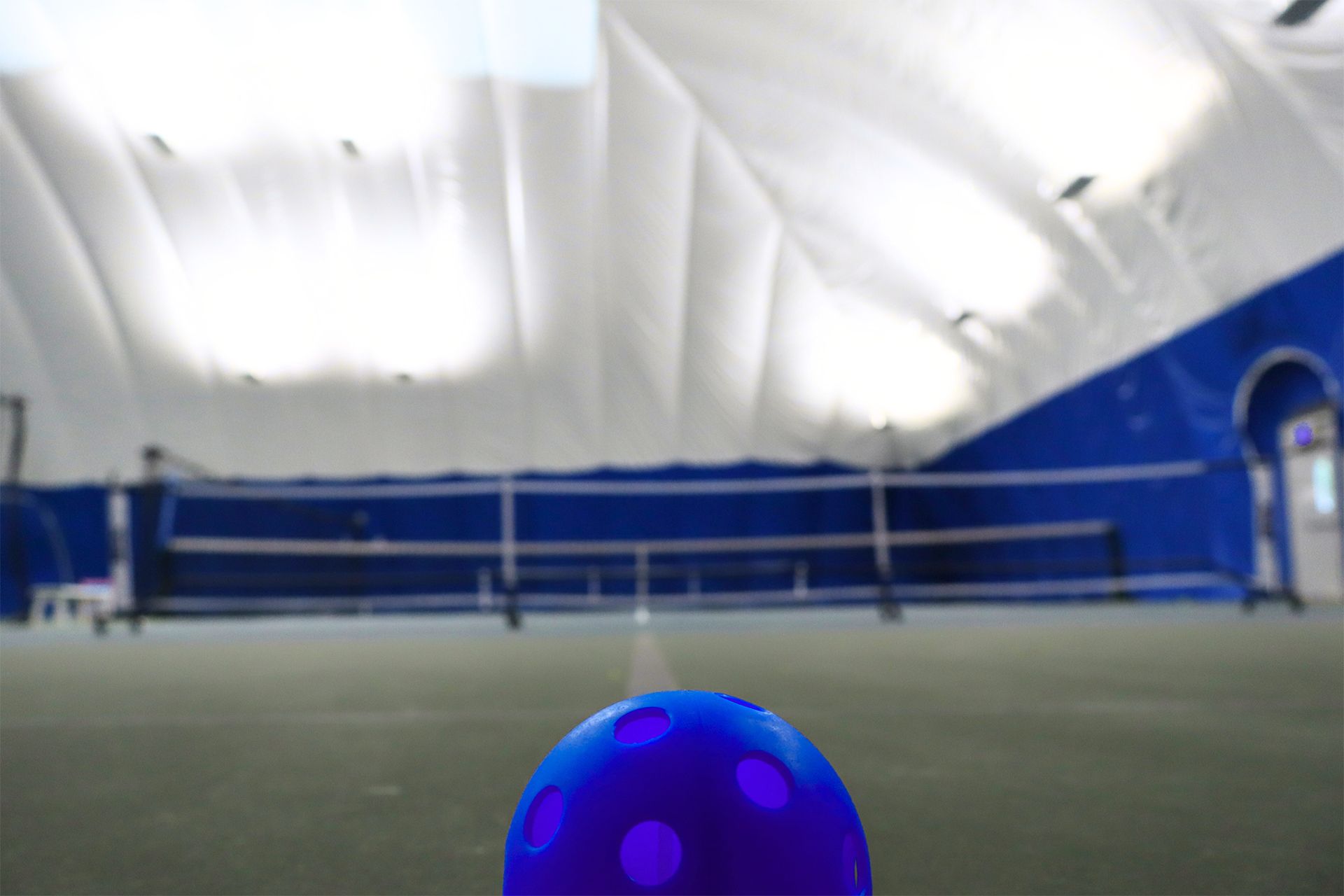 Blue ball on indoor tennis court beneath a white domed ceiling