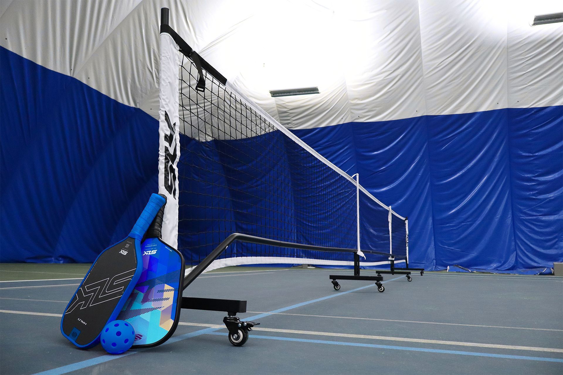 Paddleball court with net, blue-and-white walls, and two paddles leaning on the floor