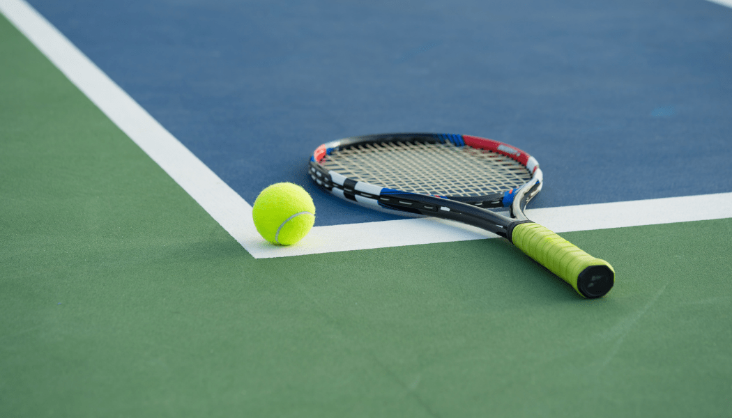 A tennis racket and ball are on a tennis court.