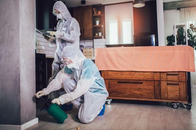 Two people in white protective suits cleaning a home interior with spray and tools.