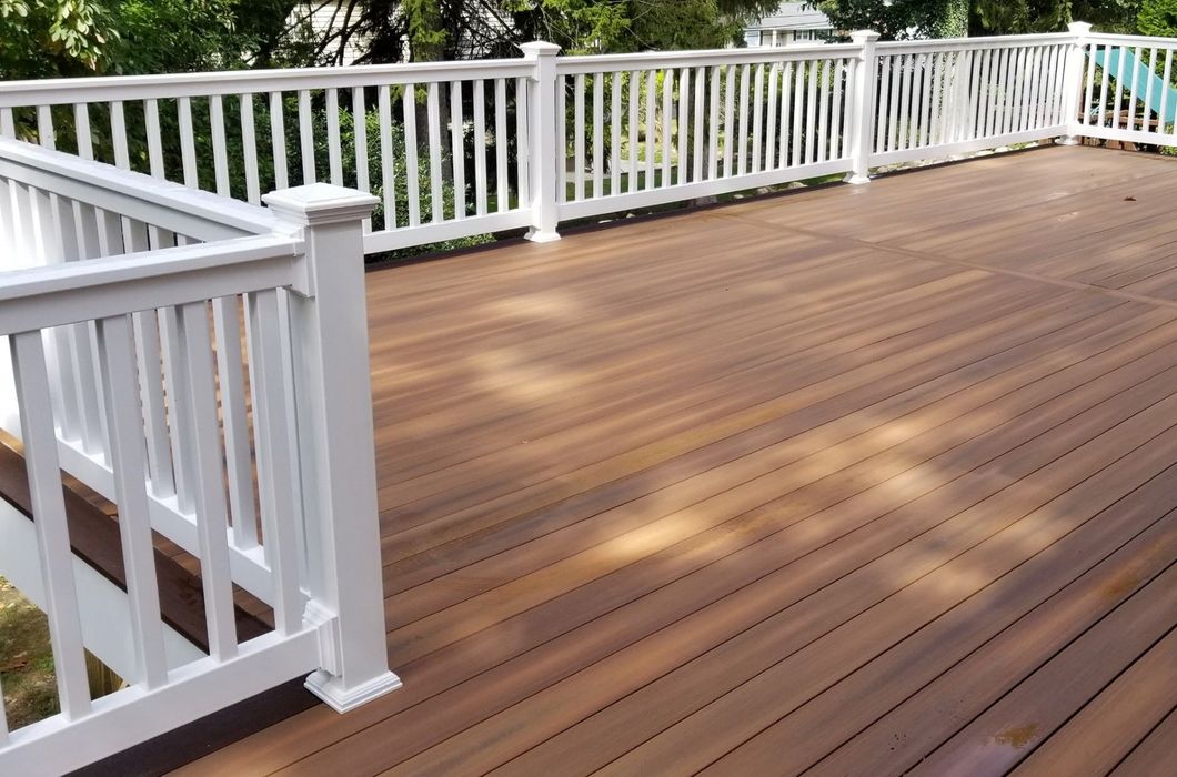 Wooden deck with white railings and stairs, overlooking greenery