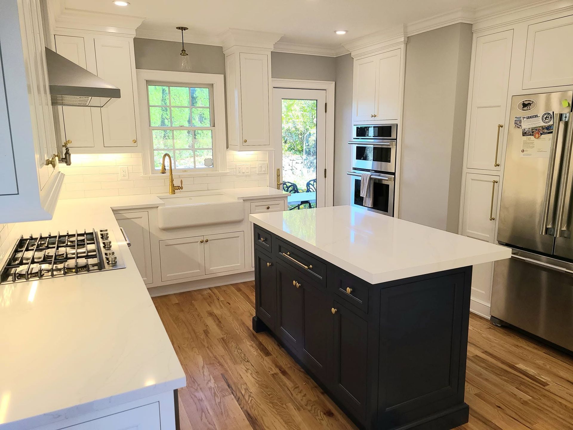 Bright white kitchen with dark island, stainless steel appliances, and hardwood floors