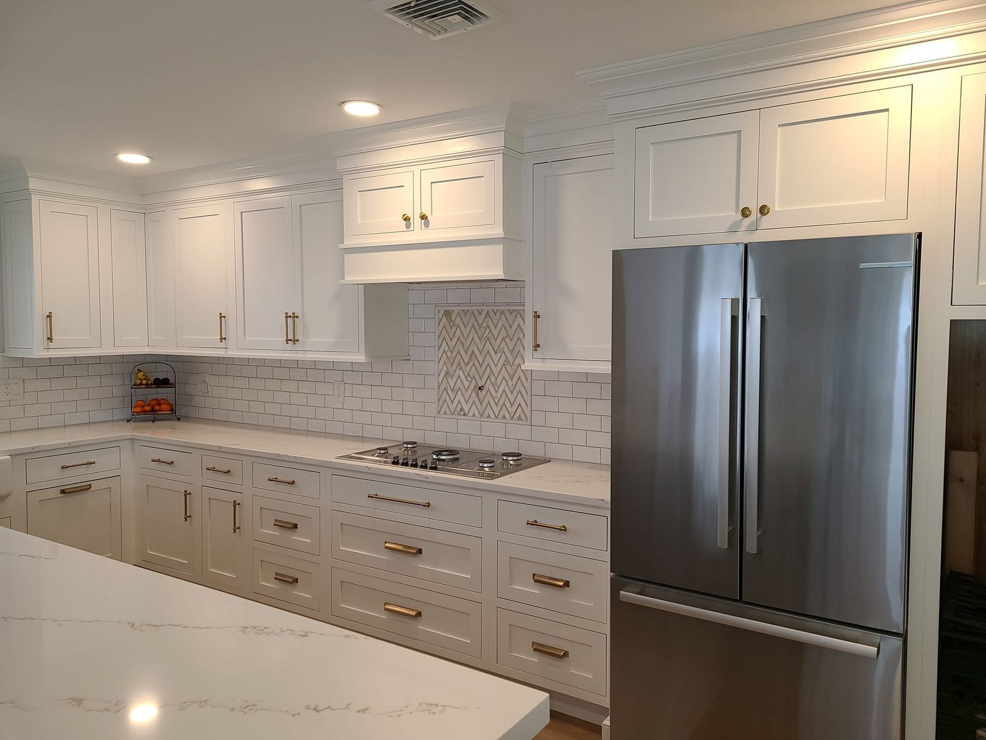 Bright white modern kitchen with stainless steel refrigerator, marble counters, and light tile backsplash