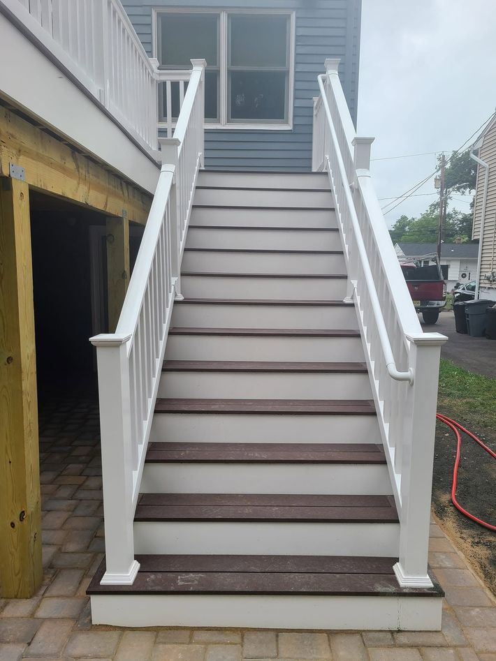 White exterior staircase leading to a gray deck, with white railings and brown stair treads. White exterior staircase leading to a gray deck, with white railings and brown stair treads.