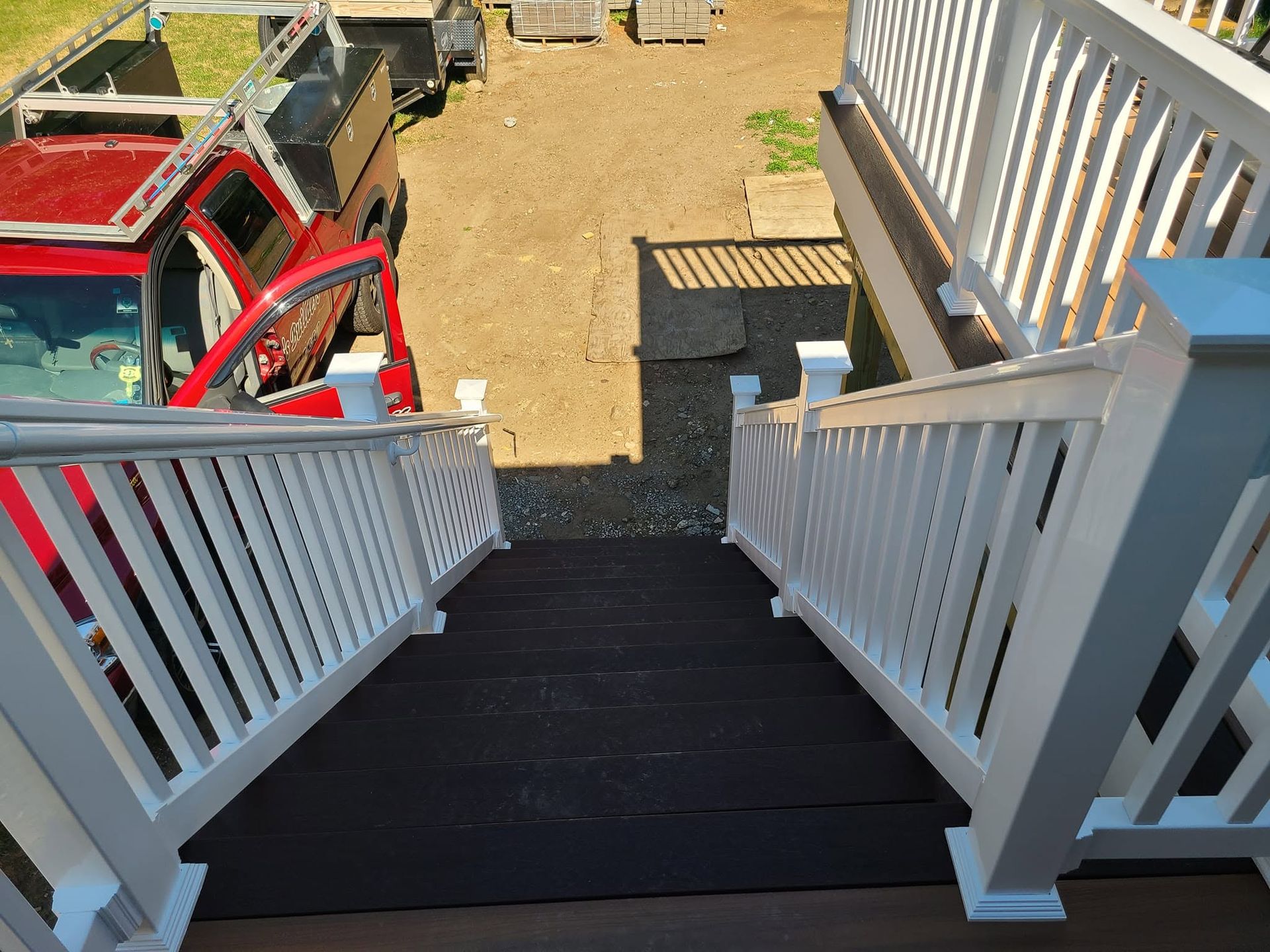 White-railed stairs descending to a gravel yard with a red truck and tools below