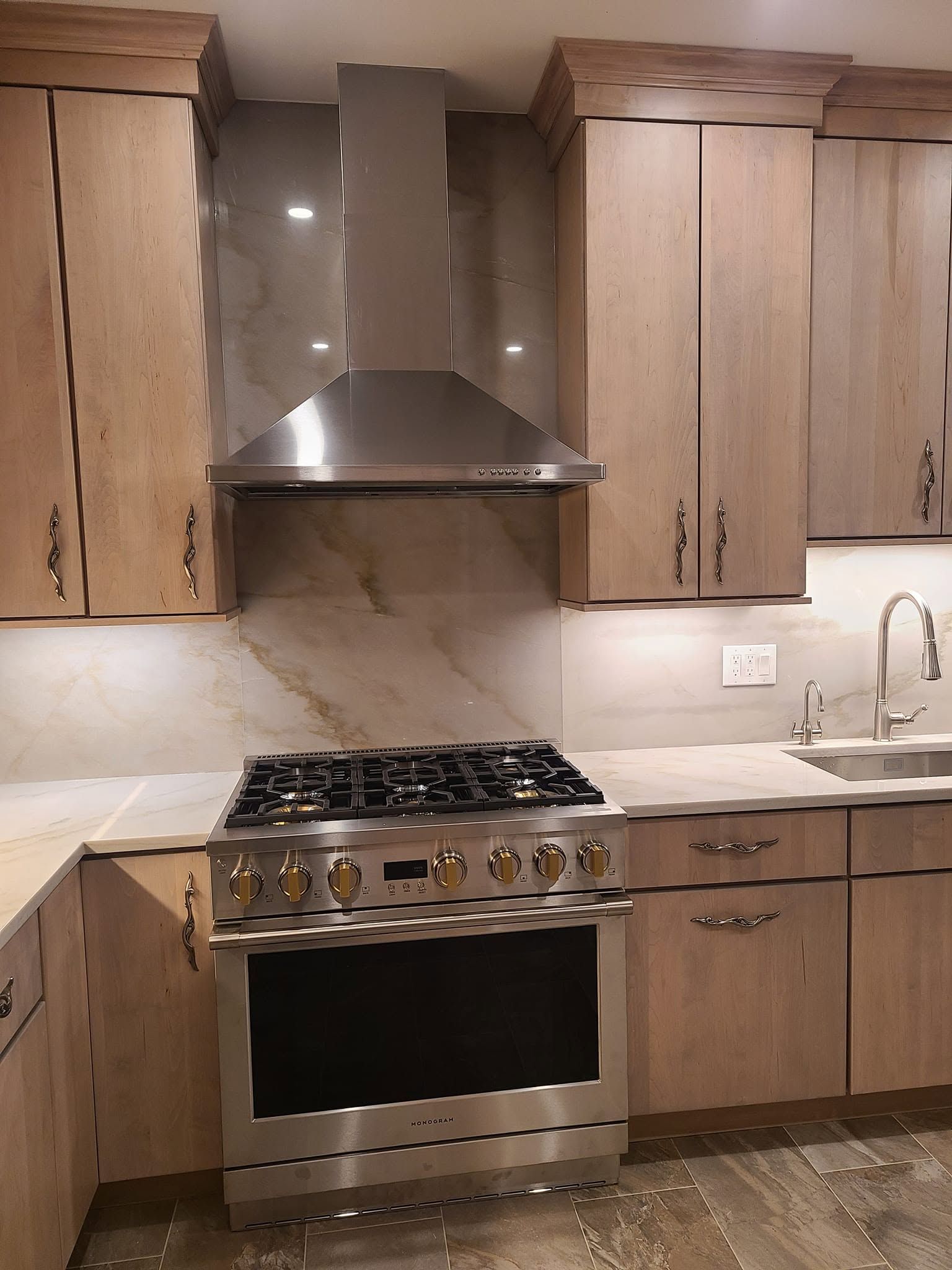 Modern kitchen with wood cabinets, stainless steel range and hood, and marble backsplash and countertop.