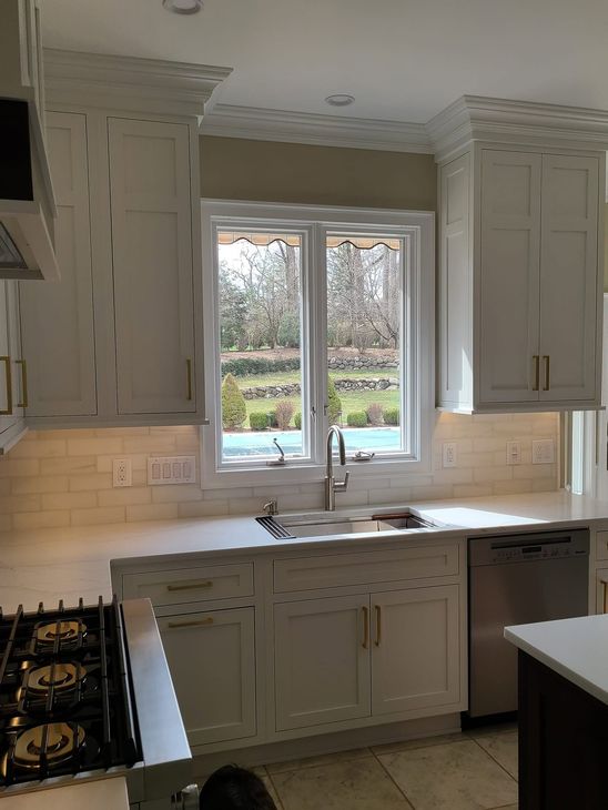 Bright white kitchen with double window above a sink, cream cabinets, and a gas stove on the left. Bright white kitchen with double window above a sink, cream cabinets, and a gas stove on the left.