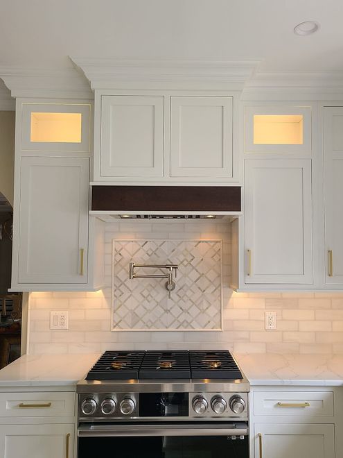 White kitchen with gas range, marble backsplash, and lit glass-front cabinets above the stove White kitchen with gas range, marble backsplash, and lit glass-front cabinets above the stove