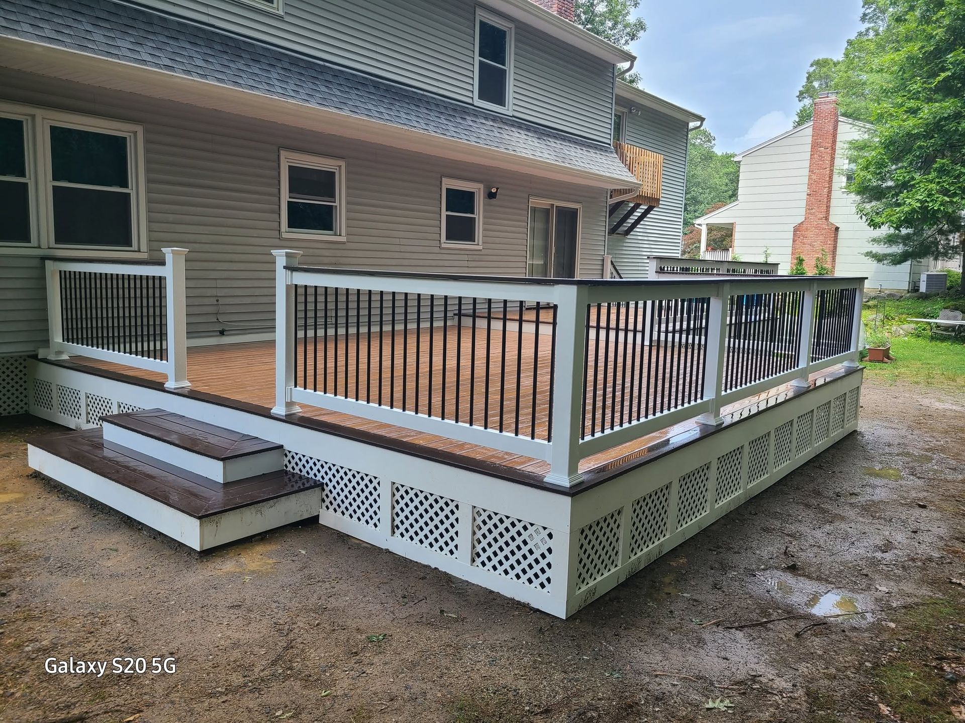 Small raised wooden porch deck with white railing attached to a house, with steps and lattice skirting.