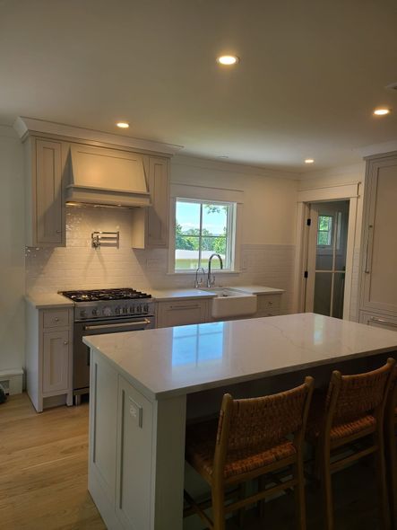Bright kitchen with white island, wicker stools, stove, sink, and daylight through windows. Bright kitchen with white island, wicker stools, stove, sink, and daylight through windows.