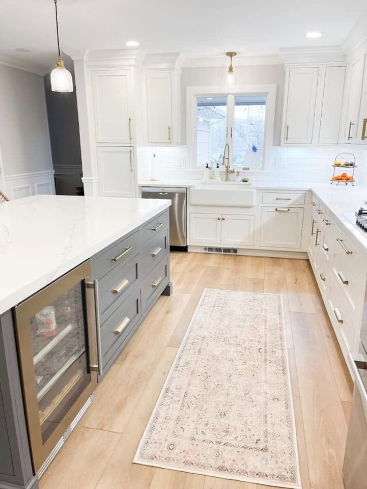 Bright modern white kitchen with gray island, light wood floors, and a runner rug.