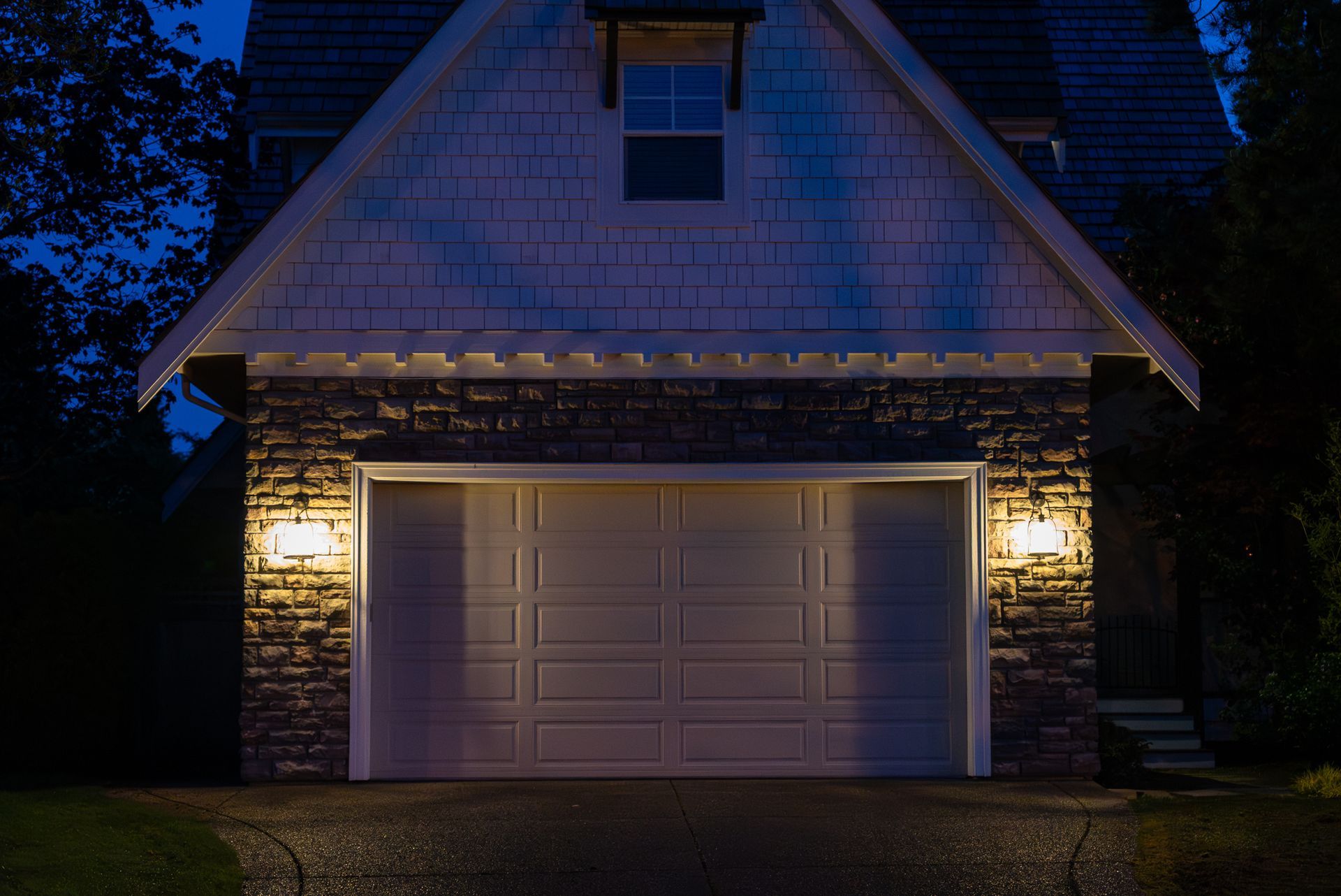 Dimly lit house garage at night with warm porch lights and a closed white door