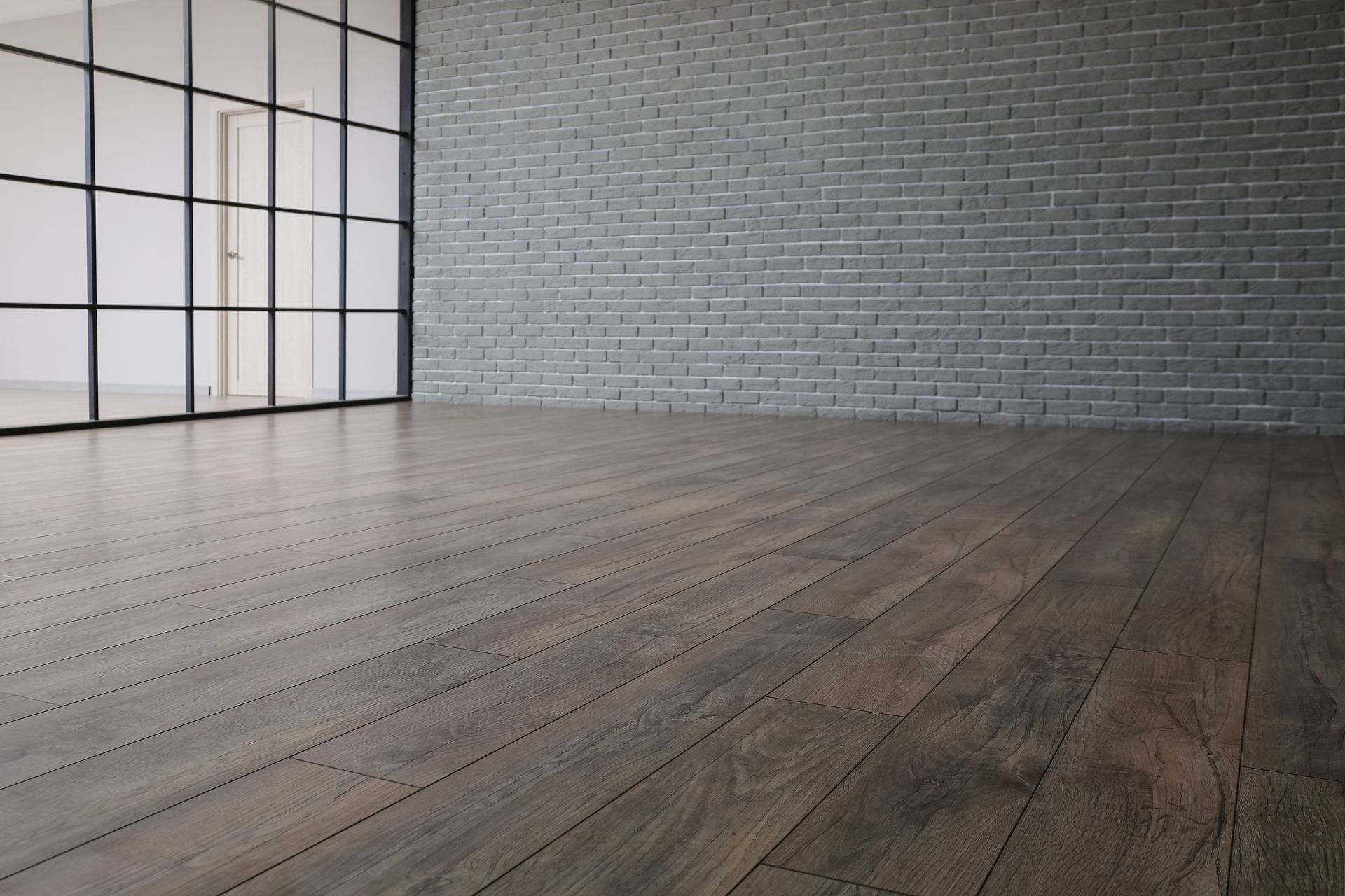 Empty modern room with wood floor, gray brick wall, and large black-framed windows Empty modern room with wood floor, gray brick wall, and large black-framed windows