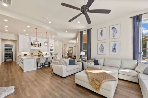 Bright open-plan living room and kitchen with white sofas, wood floors, ceiling fan, and framed wall art Bright open-plan living room and kitchen with white sofas, wood floors, ceiling fan, and framed wall art