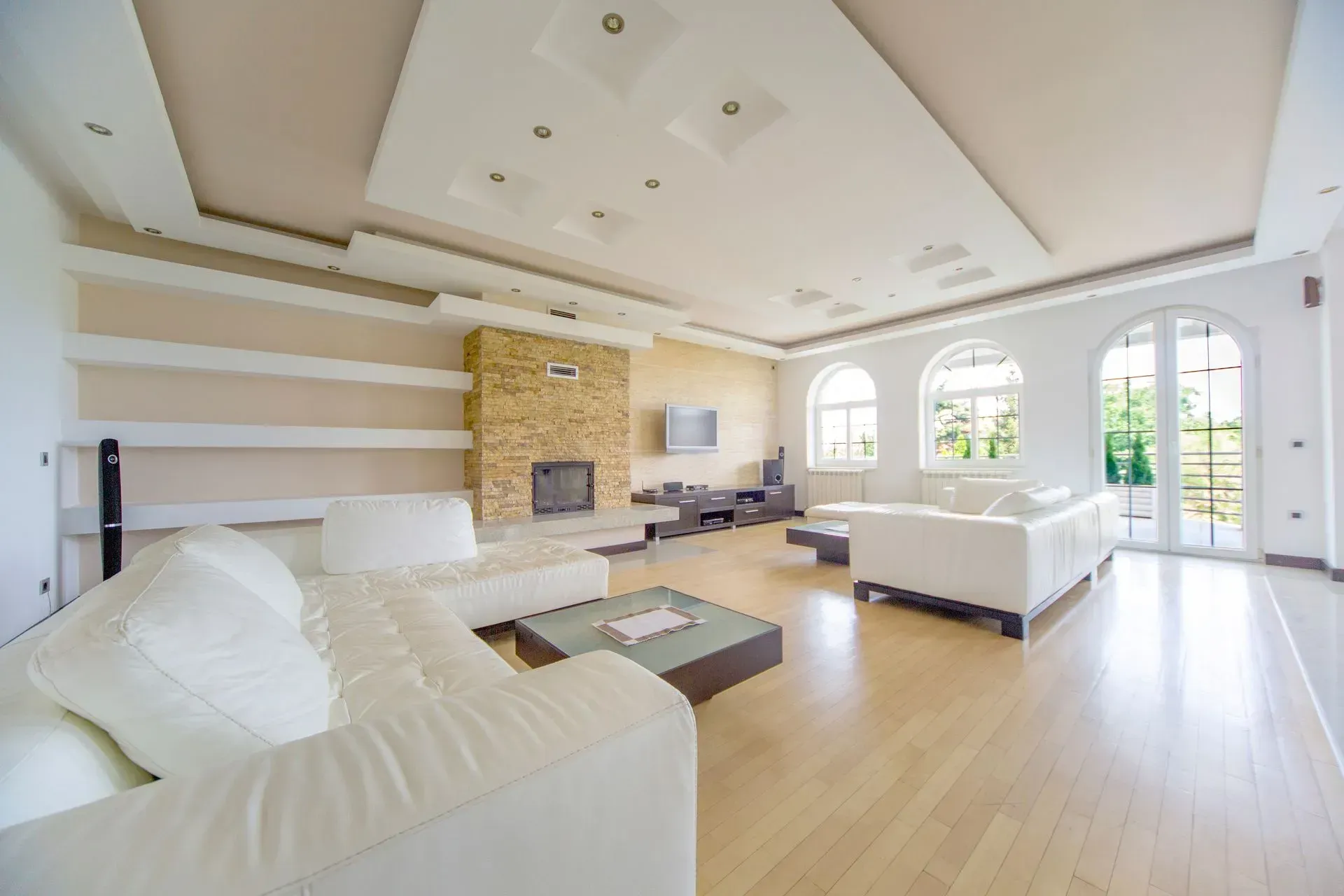 Bright modern living room with white sofas, fireplace, wood floors, and large arched windows Bright modern living room with white sofas, fireplace, wood floors, and large arched windows