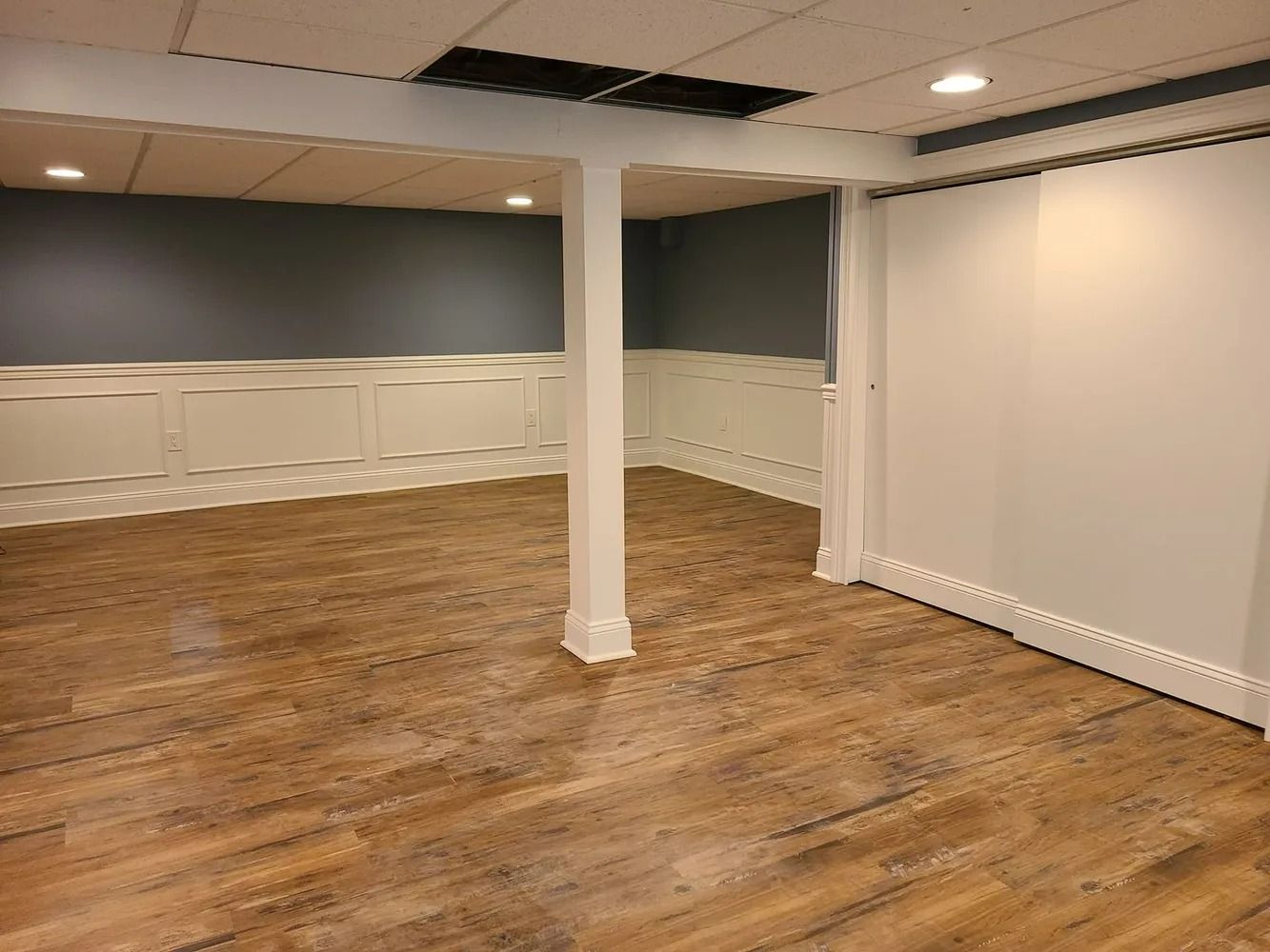 Empty basement room with wood floors, white walls, and a central support column