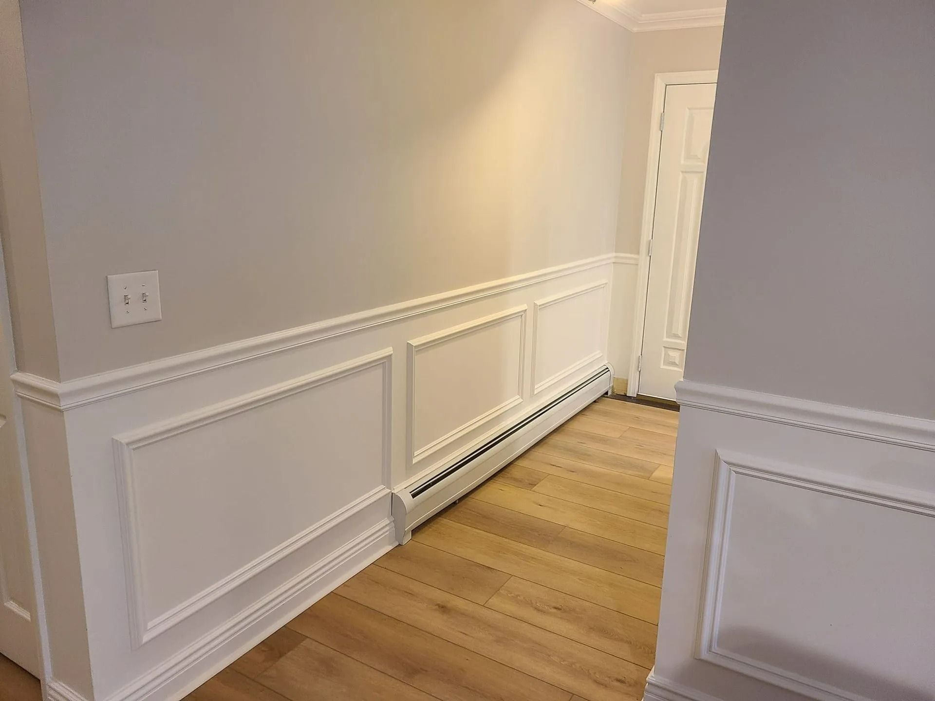 Hallway with light wood floor, white paneled walls, and a radiator along the left side