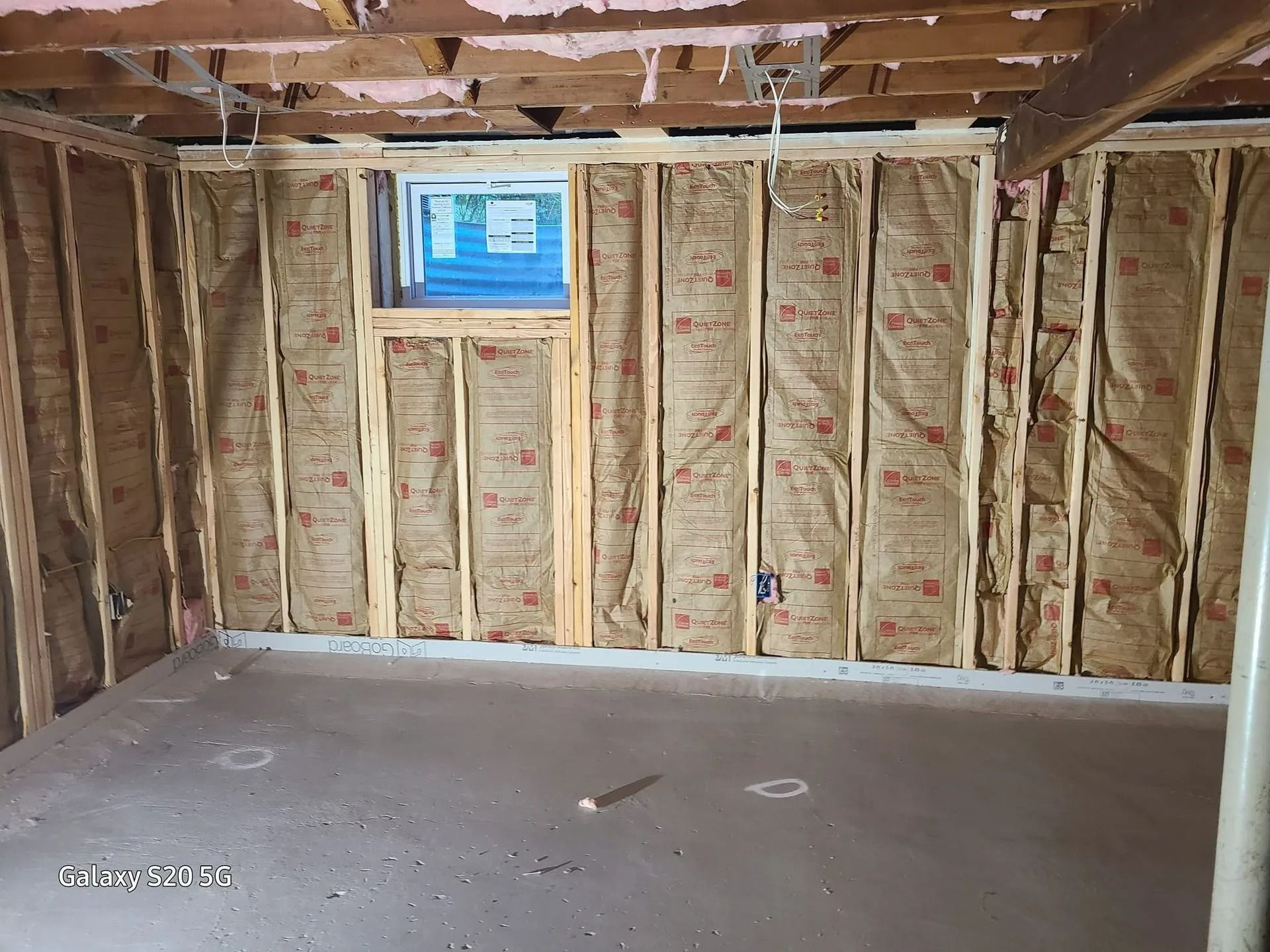 Unfinished basement with exposed insulation, a small window, and a bare concrete floor