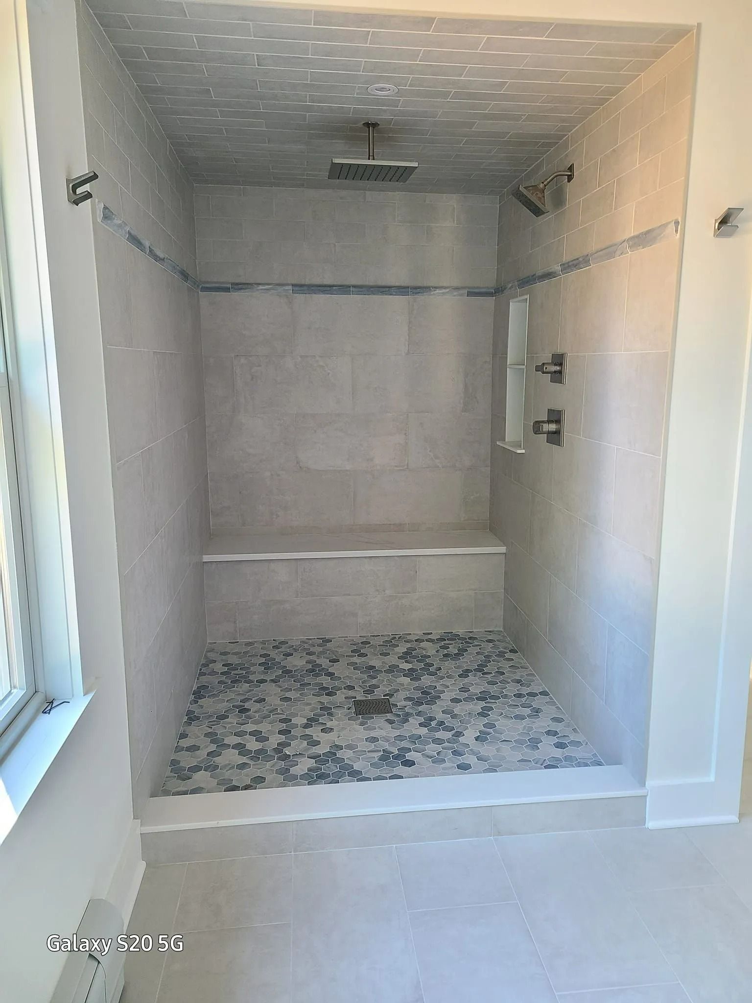 Empty tiled shower with glass window, gray walls, and white trim in a bathroom. Empty tiled shower with glass window, gray walls, and white trim in a bathroom.