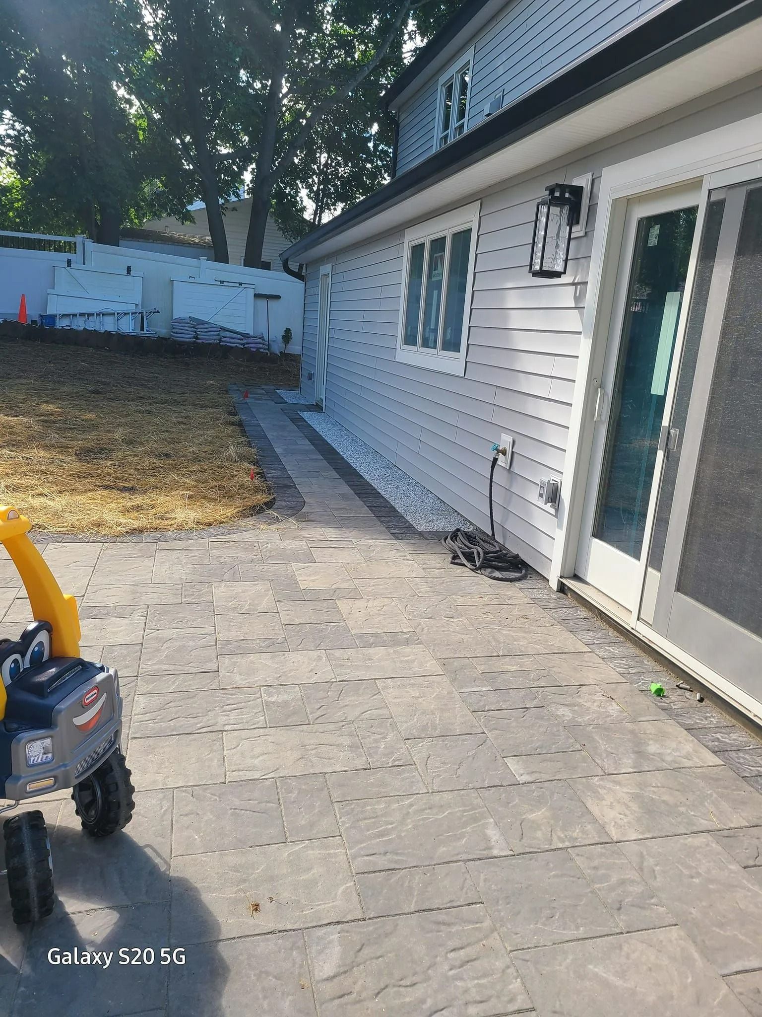 Back patio with stone pavers, white siding, and a child’s ride-on toy in the foreground